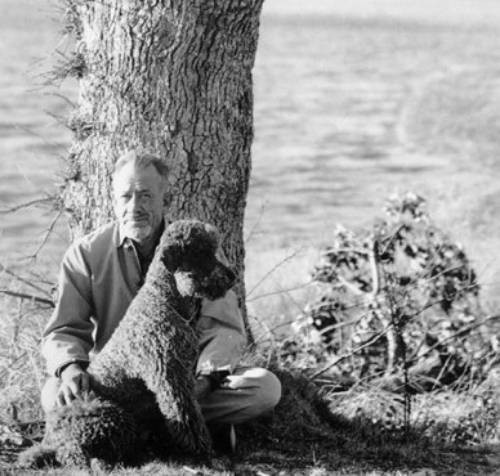 Charley the poodle, John Steinbeck's travel companion in "Travels with Charley," sits beside the author, illustrating their close bond during their cross-country journey.