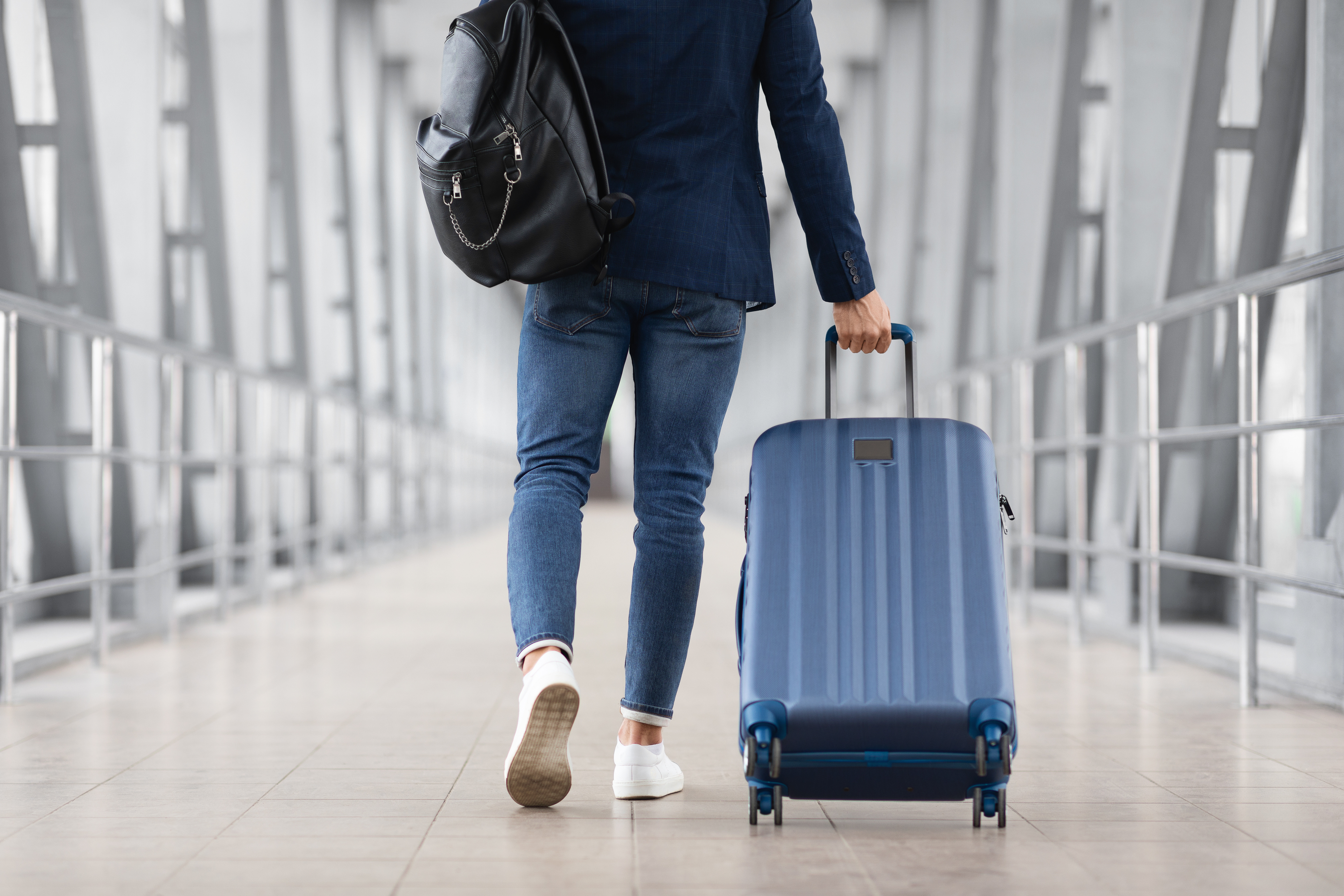 Một người đàn ông không thể nhận ra đang mang một chiếc túi và vali đi về phía cổng lên máy bay trong một nhà ga sân bay