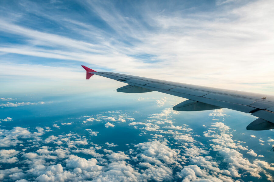 Máy bay bay trên bầu trời xanh với những đám mây trắng, minh họa cho việc onward travel bằng đường hàng không
