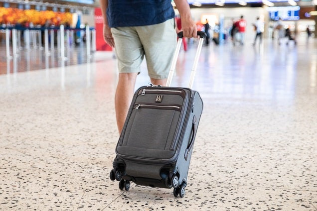 Một người đàn ông đang đi bộ trong sân bay với chiếc ba lô Travelpro Platinum Elite.