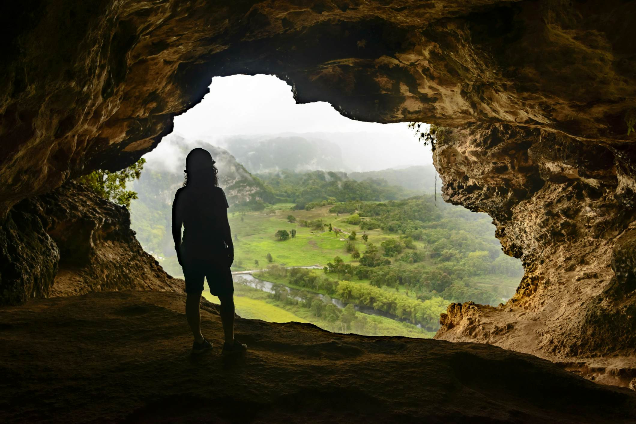 Một người đàn ông đứng trong hang động nhìn ra thung lũng xanh tươi bên dưới ở Puerto Rico