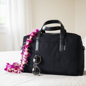 Away The Everywhere Bag trên giường với kính râm tựa vào túi.