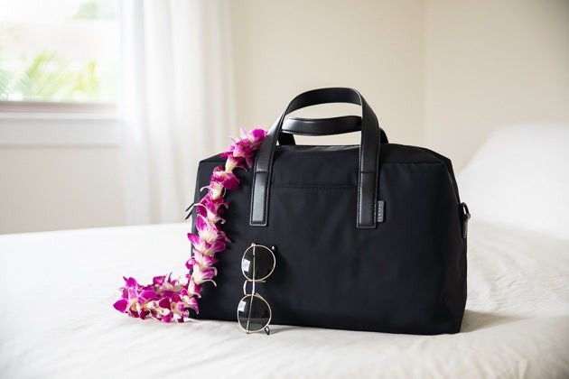 Away The Everywhere Bag trên giường với kính râm đặt cạnh túi.