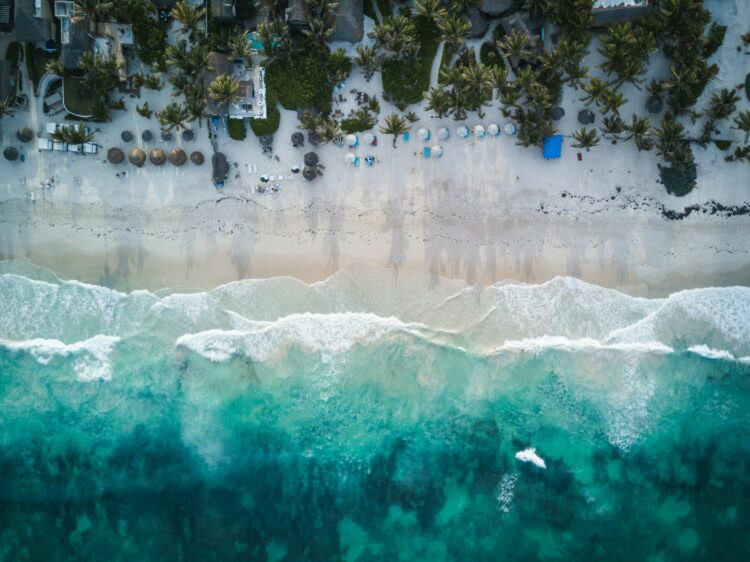 Toàn cảnh bãi biển cát trắng nguyên sơ và làn nước màu ngọc lam của Tulum, với hàng cọ và khu nghỉ dưỡng sang trọng bên bờ biển—hoàn hảo cho một chuyến đi chơi sinh nhật lần thứ 30.